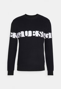 Sweat-shirt noir à manches longues avec des lettres blanches en bloc formant une bande horizontale sur la poitrine et les manches.