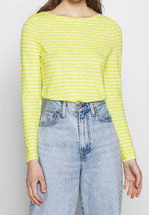 Kvinde iført en gul- og hvidstribet langærmet top stoppet ned i højtaljede lyseblå denimjeans.