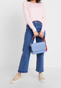 Suéter rosa claro combinado con jeans de pierna ancha de mezclilla azul de cintura alta. Sosteniendo un bolso cruzado azul claro con una correa de patrón colorido.