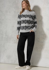Grijze trui met zwart geometrisch patroon, ronde hals, lange mouwen, gecombineerd met zwarte wijde broek en witte sneakers. Gestructureerde stof.