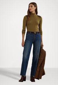 Col roulé en maille olive avec des accents aux épaules, jean bleu taille haute avec un bouton, associé à des bottines à talons marron et un blazer marron.
