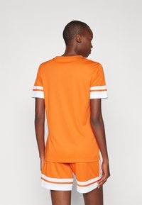 Oranje sportshirt met witte accenten en korte mouwen, gecombineerd met bijpassende oranje shorts met witte strepen. Zachte, ademende stof.