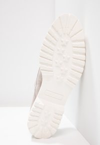 Sneaker con una morbida tomaia in suede grigio chiaro e una suola in gomma bianca testurizzata. La suola presenta un motivo a stella e un design a righe.