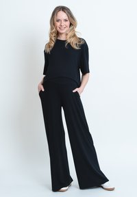 Svart, löst sittande topp med korta ärmar och vida svarta byxor. Slät tyg med framfickor. Vita sneakers kompletterar outfiten.