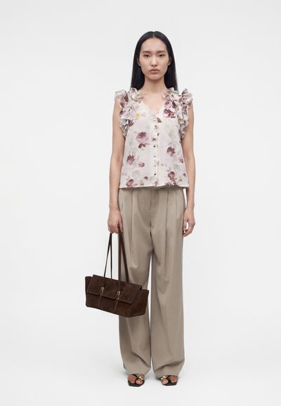 Γυναίκα που φοράει αμάνικο, φλοράλ μπλουζάκι με βολάν, μπεζ παντελόνια με φαρδιά πόδια, μαύρα σανδάλια και κρατάει καφέ τσάντα με αγκράφες.