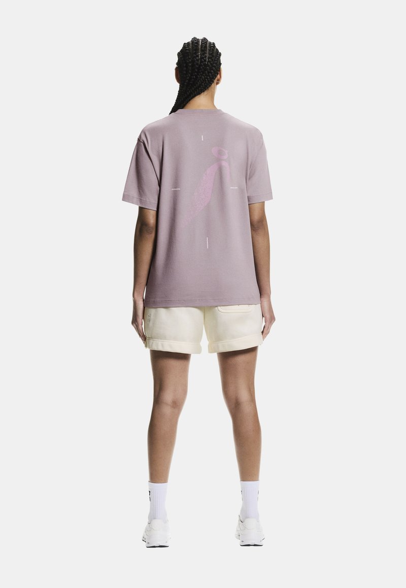 T-shirt en coton lavande avec un grand motif rose au dos, associé à un short crème. Manches courtes et coupe décontractée.