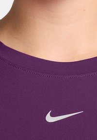 Fialové sportovní triko vyrobené z hladkého materiálu, s kulatým límcem a bílým logem Nike na přední straně. Jsou viditelné ploché švy.