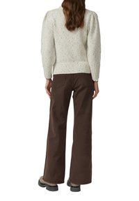 Dikke crèmekleurige gebreide trui met textuurafwerking en geribde zoom, gecombineerd met brede bruine broek met een relaxte pasvorm en achterzakken.