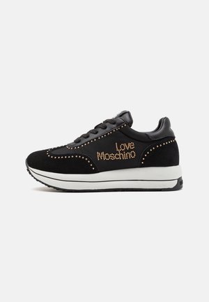 Baskets noires avec semelle blanche, détails de clous dorés et texte "Love Moschino" sur le côté, montrées de profil sur fond blanc.