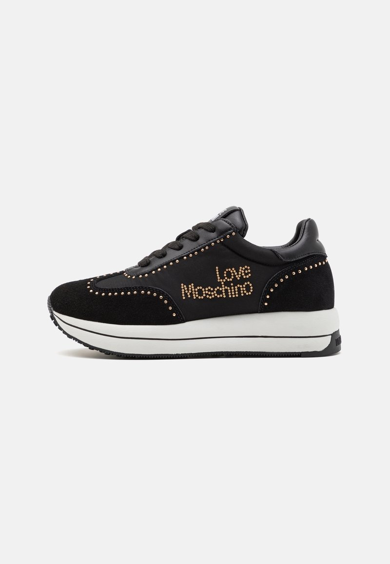 Baskets noires avec semelle blanche, détails de clous dorés et texte "Love Moschino" sur le côté, montrées de profil sur fond blanc.