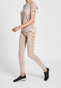 Top deportivo beige con mangas cortas texturizadas y rayas horizontales; los leggings a juego presentan patrones en forma de chevron. Zapatos deportivos negros completan el conjunto.