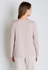 Jasnoróżowa bluzka z długim rękawem i szerokim dekoltem, zestawiona z jasnymi spodniami w wzory z drobnymi motywami. Miękki materiał, casualowy styl.