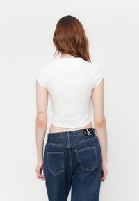 Witte cropped t-shirt met korte mouwen, gecombineerd met donkerblauwe denim jeans met een zichtbaar logo op de tailleband en achterzakken.