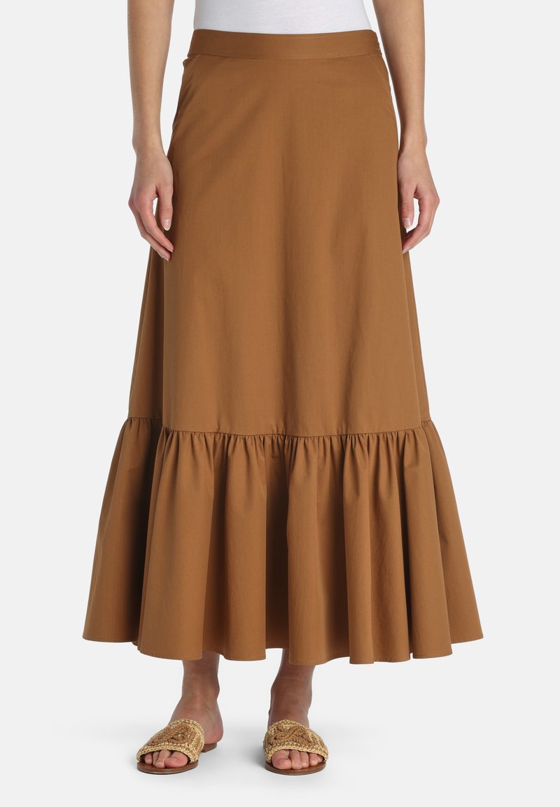 Brown ankle-length skirt with a gathered ruffle hem worn with woven slide sandals and a white top, shown from waist to feet.