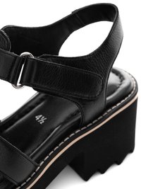Black leather platform sandal with adjustable ankle strap, cushioned insole marked size 4½, and chunky ridged sole with side stitching detail.
