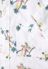 Koszula z krótkim rękawem z białej bawełny z kolorowym tropikalnym nadrukiem przedstawiającym palmy, flamingi i ananasy. Zapinana na guziki z kieszonką.