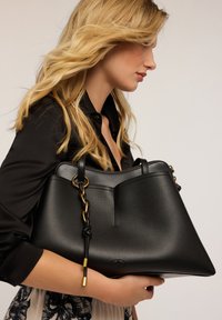 Borsa a mano in pelle nera texturizzata con un design strutturato, dotata di hardware in tonalità oro, un'accenno a catena e doppie maniglie superiori.