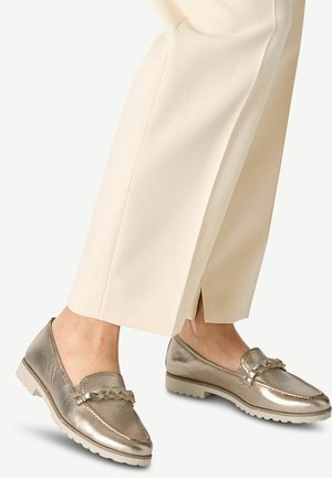 Metallic loafer shoes with braided detail worn with cream-colored cropped trousers.
