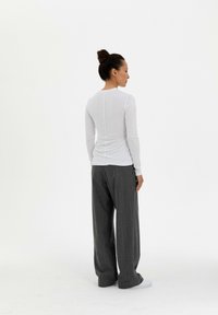 Wit long-sleeve top met een ronde hals, gecombineerd met grijs, gestreepte wijde broek en witte sneakers, gezien vanaf de achterkant.