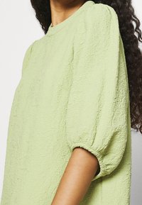 Haut texturé vert lime avec un col rond, des manches courtes bouffantes et une finition en tissu doux et froissé.