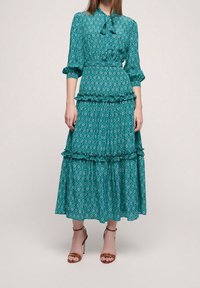 Robe midi à motifs teal avec un ourlet volanté, une ceinture à la taille et des manches longues. Présente un motif en losange et une texture de tissu douce.