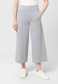 Lichtgrijze, wijde broek van zachte stof, met een elastische tailleband en zijzakken, gecombineerd met witte sneakers.