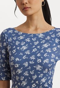 Top in cotone blu con scollatura ampia e maniche corte. Presenta un motivo floreale bianco, con fiori di dimensioni variabili su tutta la stoffa.