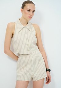 Korte mouwen top en shorts set in lichtbeige stof met verticale strepen, voorzien van een brede kraag en knopen aan de voorkant.