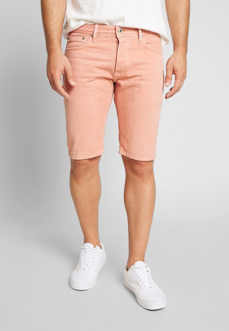 Shorts de mezclilla rosa claro con corte recto, que cuentan con cinco bolsillos, pasadores para cinturón y un dobladillo sin rematar, combinados con zapatillas blancas.