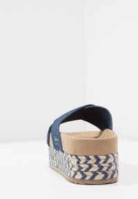 Blå tygplattformssandal med beigefärgad mockaskinnsinnersula och vävd jutesula i blå och naturliga nyanser, visad från baksidan.