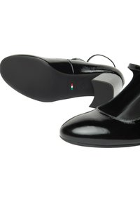 Tacchi in vernice nera con punta arrotondata e cinturino alla Mary Jane, dotati di una suola testurizzata e di un accentuazione bianca sul tallone.