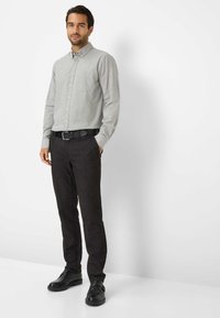 Camicia grigia chiaro con taschino, abbinata a pantaloni grigi scuri e scarpe nere. Tessuto strutturato, vestibilità sartoriale, stile casual.