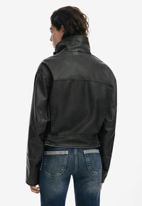 Black faux leather jacket with a high collar, cropped design, and visible stitching details. Worn over blue jeans.