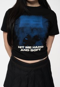 Black cotton t-shirt featuring a blue graphic design and the text "HIT ME HARD AND SOFT" in white, with a cropped fit.