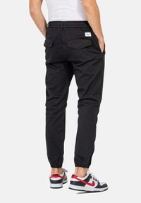 Pantalones jogger negros con cintura elástica y puños, que cuentan con dos bolsillos traseros. Llevados con zapatillas negras y blancas con acentos rojos.