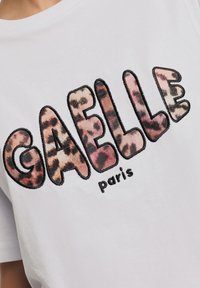 T-shirt bianco in cotone con grande e vivace lettering "GAELLE" in una fantasia leopardata, con delicate cuciture che delineano il testo.