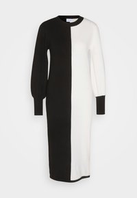 Stickad klänning med svart och vit split-design, med långa puffärmar och rund halsringning. Mjuk textur och knälång skärning.
