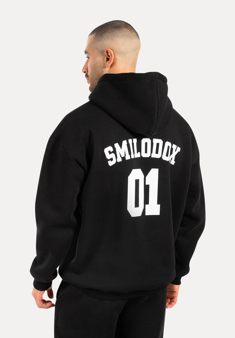 Czarna bluza z kapturem z białym napisem "SMILODOX 01" na plecach. Wykonana z miękkiego, teksturowanego materiału o luźnym kroju i ściągaczach przy mankietach.