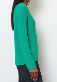 Pull en tricot vert avec un motif texturé, manches longues et coupe décontractée. Il possède des poignets côtelés et un col arrondi.