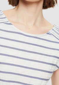 Top blanco con rayas horizontales azules, textura suave, escote redondo y detalles plisados en los hombros. Diseño casual adecuado para clima cálido.