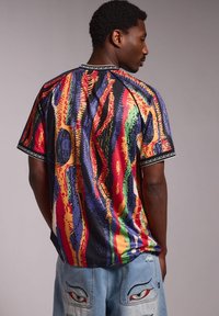 Camisa de manga corta colorida con un vibrante patrón abstracto en rojo, verde, azul y amarillo, con un borde negro alrededor del cuello.