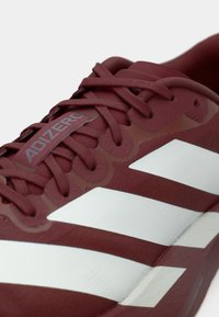 Κόκκινο αθλητικό παπούτσι με λευκές ρίγες, υφή στην επάνω επιφάνεια, επενδεδυμένη σόλα και ετικέτα με λογότυπο. Διαθέτει κορδόνια για ασφαλή εφαρμογή.