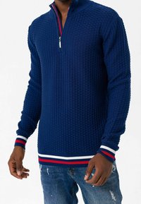 Maglione pullover blu navy con motivo testurizzato, collo a zip a un quarto e polsini a righe con coste. Realizzato in tessuto lavorato a maglia.