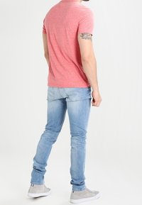 Röd melerad kortärmad t-shirt, ljusblå skinny jeans, grå sneakers. Outfiten visar en avslappnad, figursydd stil med minimalistisk design.