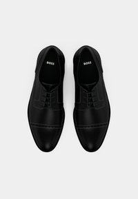 Pár čiernych lesklých kožených spoločenských topánok so šnúrkami a značkou "BOSS" vo vnútri, zobrazených zhora na bielom pozadí.