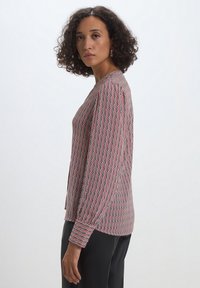 Blusa a maniche lunghe con un motivo geometrico rosso e nero, realizzata in tessuto leggero, con scollo rotondo e vestibilità rilassata.