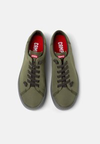 Zapatillas de lona verdes con cordones marrones oscuros, suelas de goma y plantillas rojas con la marca "CAMper". Forma clásica redondeada, diseño casual.