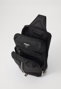 Zwarte nylon rugzak met meerdere met rits afgesloten compartimenten, voorzien van een driehoekig logo en een textuur aan de buitenkant. Interne voering met logo-patroon.
