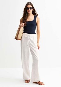 Marineblauw geribd tanktop, lichte gestreepte brede broek, bruine sandalen en een geweven schoudertas. Accessoires zijn onder andere overmaatse zwarte zonnebrillen.