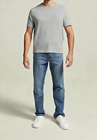 Graues T-Shirt mit kurzen Ärmeln, kombiniert mit hellblauen Jeans und weißen Sneakers. Das T-Shirt hat einen Rundhalsausschnitt und eine lockere Passform.
